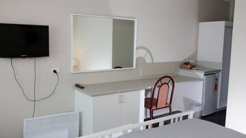 Een hotelkamer met een bed, een bureau met stoel, een televisie, een spiegel, een kleine koelkast en een verwarming.