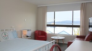 A hotel room with a bed, a red chair, a small table, and a TV.