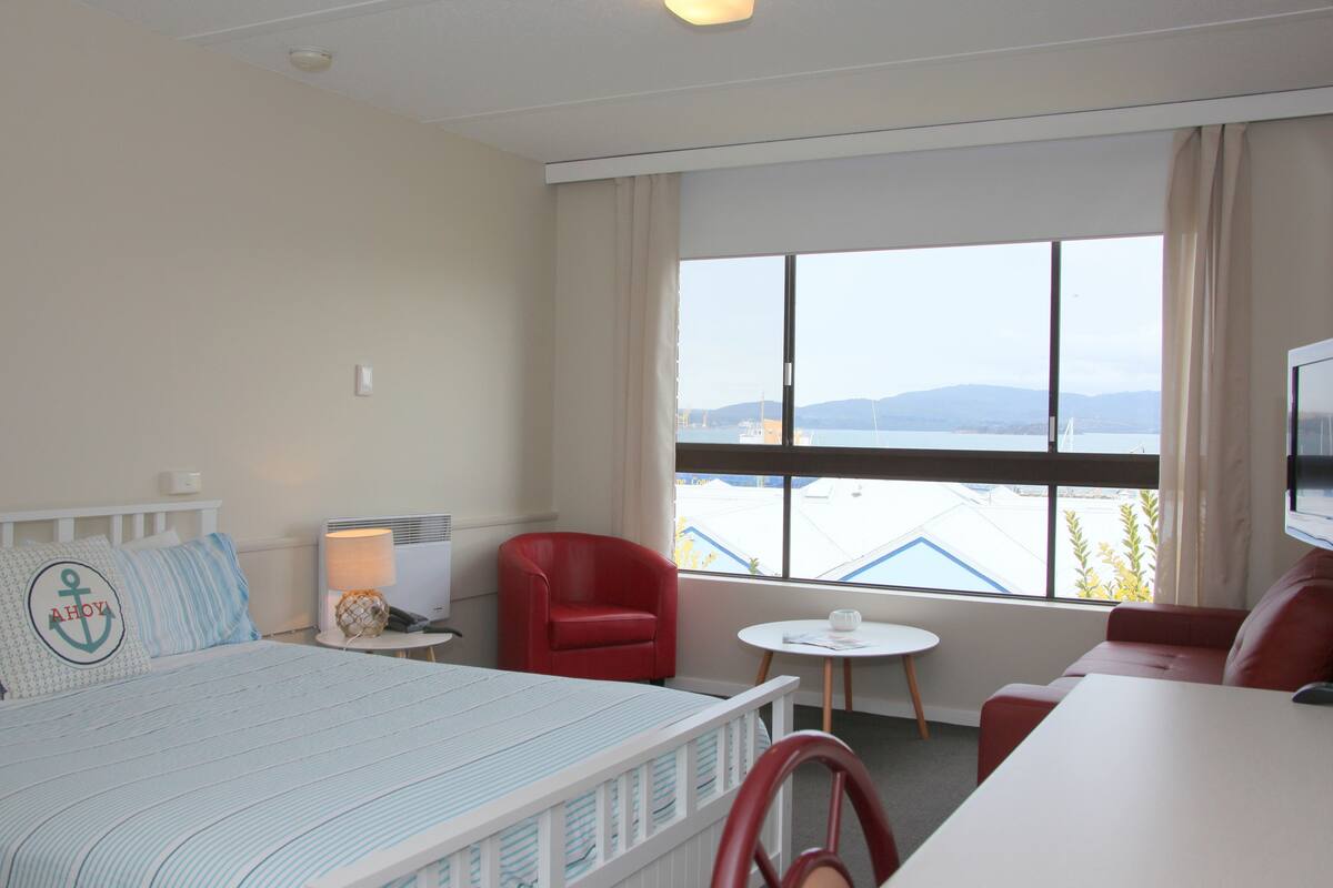 A hotel room with a bed, a red chair, a small table, and a TV.