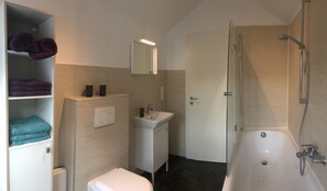 Een bad/douchecombinatie, een haardroger, handdoeken, toiletpapier