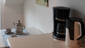 Una cocina con cafetera, tetera y una estantería con copas de vino.