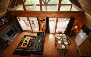 A cozy cabin interior with a fireplace, a dining area set for four, and a living room with a sofa and a TV.