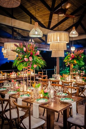 Uma área de refeições bem decorada, com mesas de madeira, toalhas de mesa brancas e pratos com padrão verde e branco.