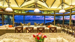 Un restaurante con vista al océano, que cuenta con una gran mesa y sillas, y un techo con diseño geométrico.