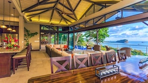 Interior moderno de hotel con área de bar, asientos con vista al mar y un amplio ventanal con vista al océano.