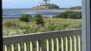 Uitzicht op de kust met een vuurtoren op een heuvel, een grasveld voor en een waterpartij.
