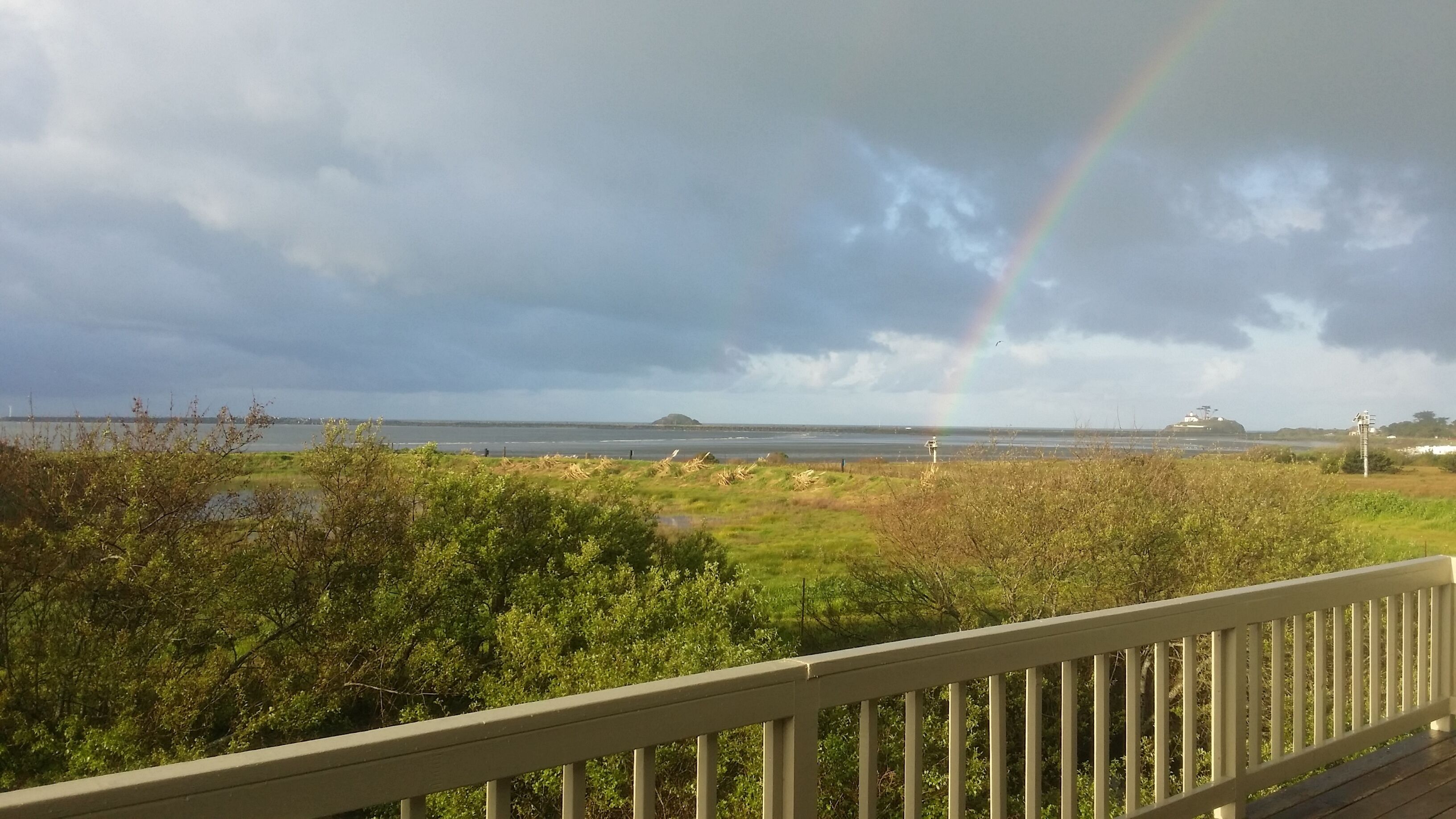 Une vue sur la côte, avec un arc-en-ciel, des zones herbeuses et une terrasse en bois.