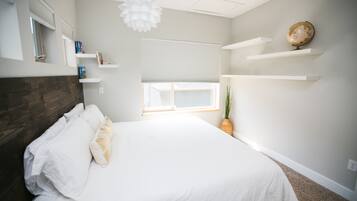 Un dormitorio con cama, paredes blancas, una ventana con persianas, cabecera de madera y un globo terráqueo en un estante.