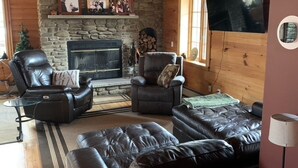 A cozy living room with a stone fireplace, leather furniture, and a mounted TV.