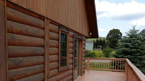 A wooden log cabin with a wooden deck and a view of the surrounding forest.