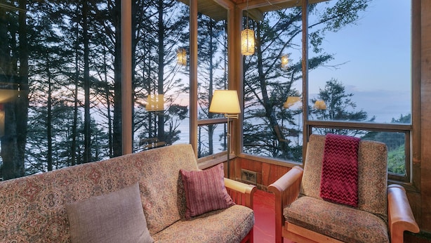 A cozy cabin interior with a large window offering a view of tall trees and a body of water.