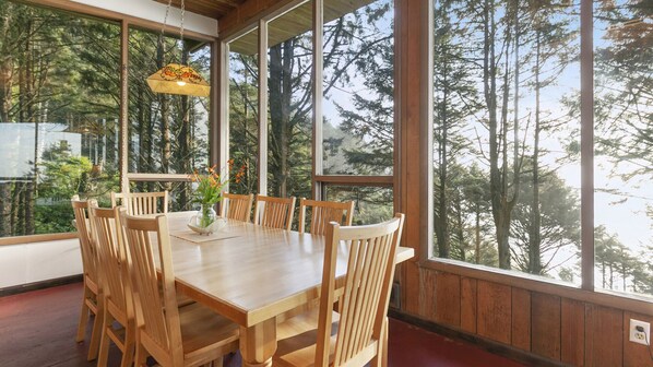 A wooden dining table with six chairs, a vase with flowers, and a hanging light fixture.