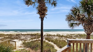 A beach view with a wooden deck, palm trees, and a sandy path leading to the ocean. - Beachside Joy 1 Bedroom Townhome Pet friendly (Panama City Beach)