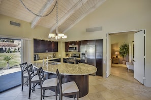 A modern kitchen with granite countertops, dark wood cabinets, stainless steel appliances, and a large island with bar stools.