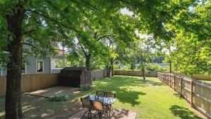 Un jardin avec une table et des chaises de patio, entouré d’arbres et d’une clôture en bois.