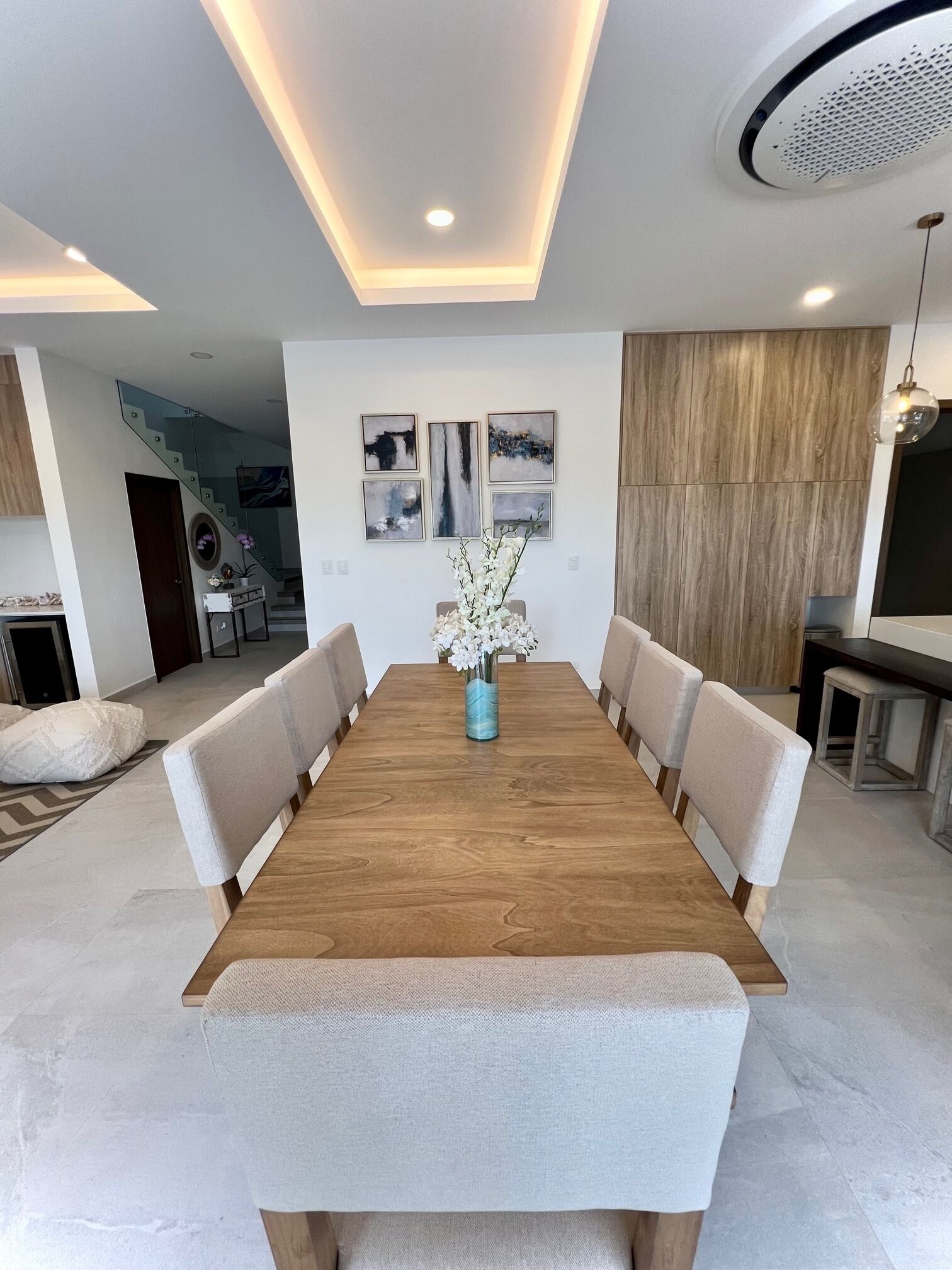 Un espace repas moderne avec une table en bois, des chaises rembourrées et un vase rempli de fleurs blanches.