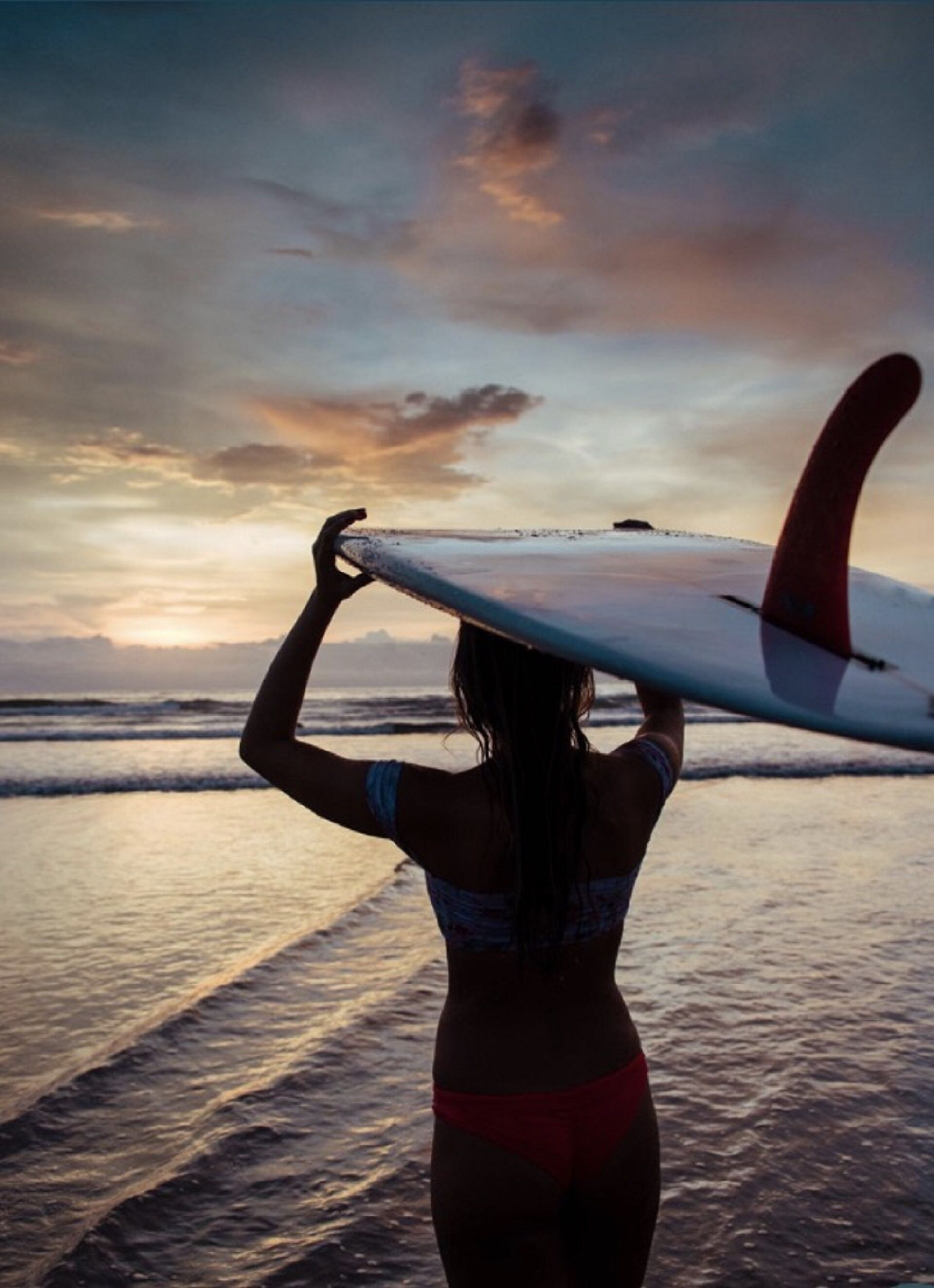Una persona sosteniendo una tabla de surf en la playa durante el atardecer.