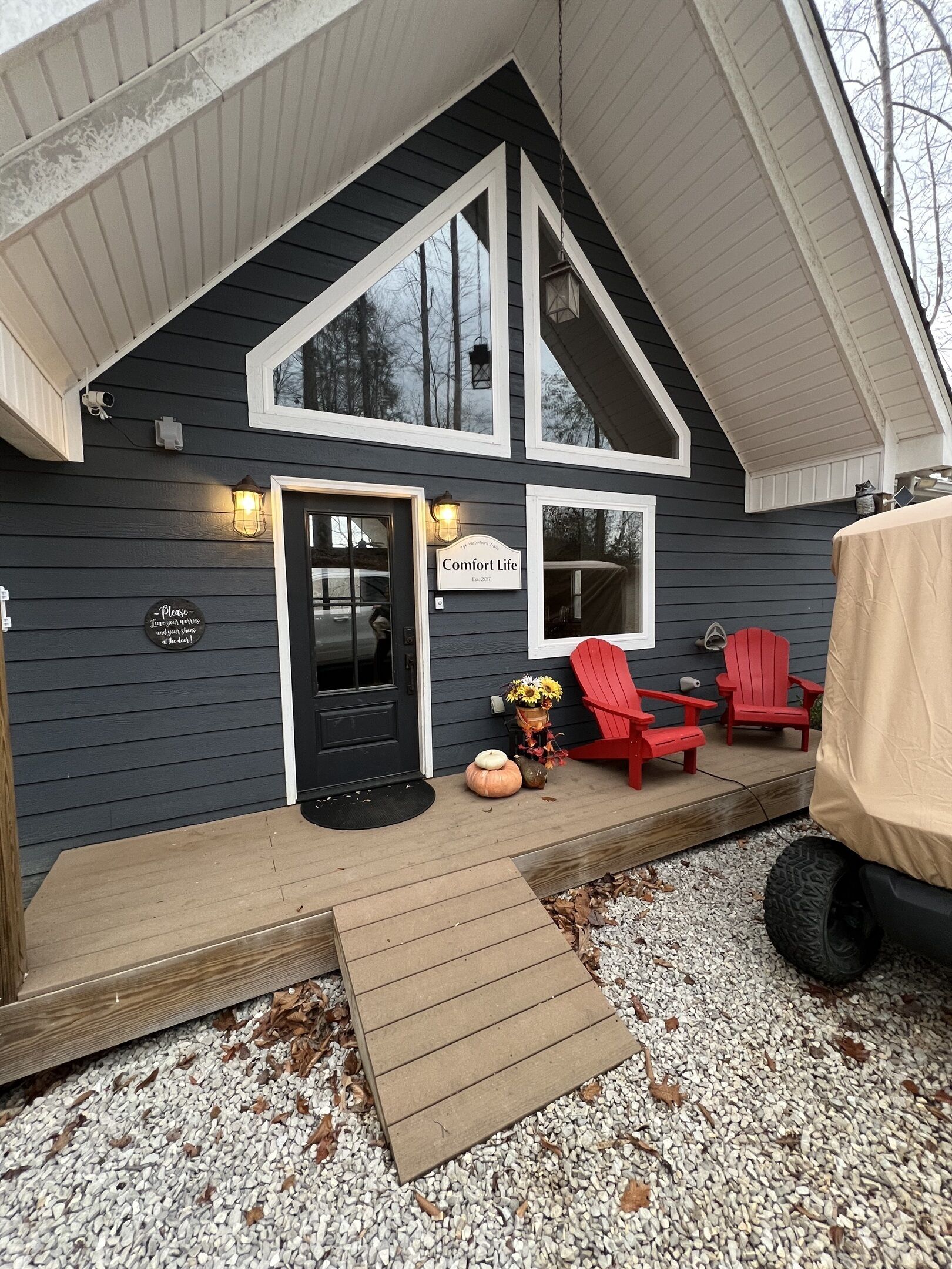A dark wooden house with a porch, a black door, and a sign that reads "Comfort Life."