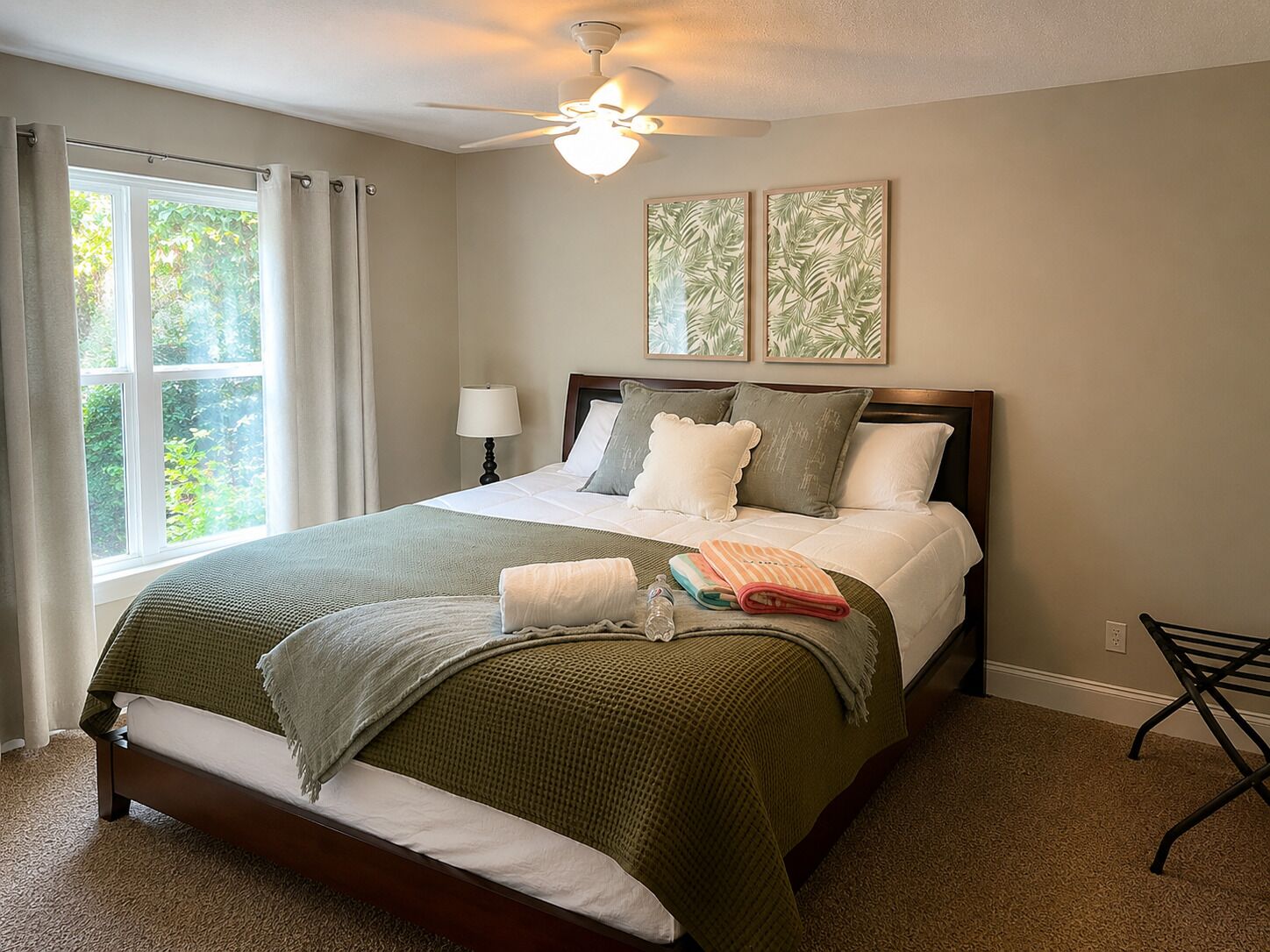 A bedroom with a bed, a ceiling fan, a window with curtains, and two framed pictures on the wall.