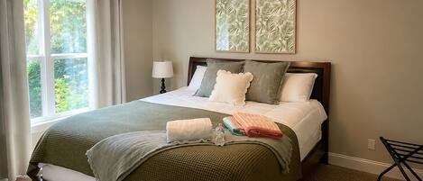 A bedroom with a bed, a ceiling fan, a window with curtains, and two framed pictures on the wall.