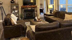 A cozy living room with a fireplace, leather sofas, a ceiling fan, and large windows. - 15% Fall Special! Lake Luxury: 6BR/6BA w/ Private Dock| Quiet Cove| (LaFollette)