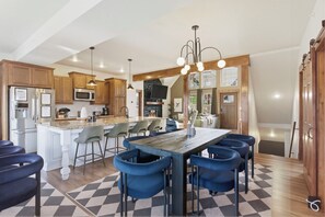 A modern kitchen with a central island, bar stools, and a dining table.