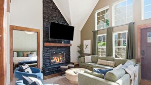 A living room with a stone fireplace, a flat-screen TV, and a large window with curtains. - Lakeview Retreat with Pool, Pickleball Court, Boat Slip, Game Room and Hot Tub (Branson)