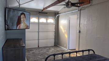 A bedroom with a bed, a ceiling fan, a painting on the wall, and a garage door.