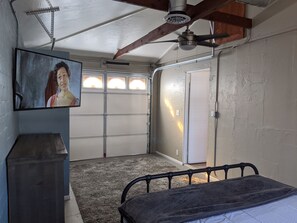 Una camera da letto con un letto, una ventola a soffitto, un quadro appeso al muro e un portone di garage.