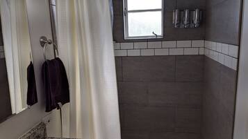 A bathroom with a shower, a sink with a marble countertop, a mirror, and a window.