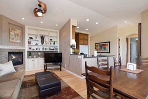 A modern living room with a fireplace, a TV, and a dining area with wooden chairs and a table.
