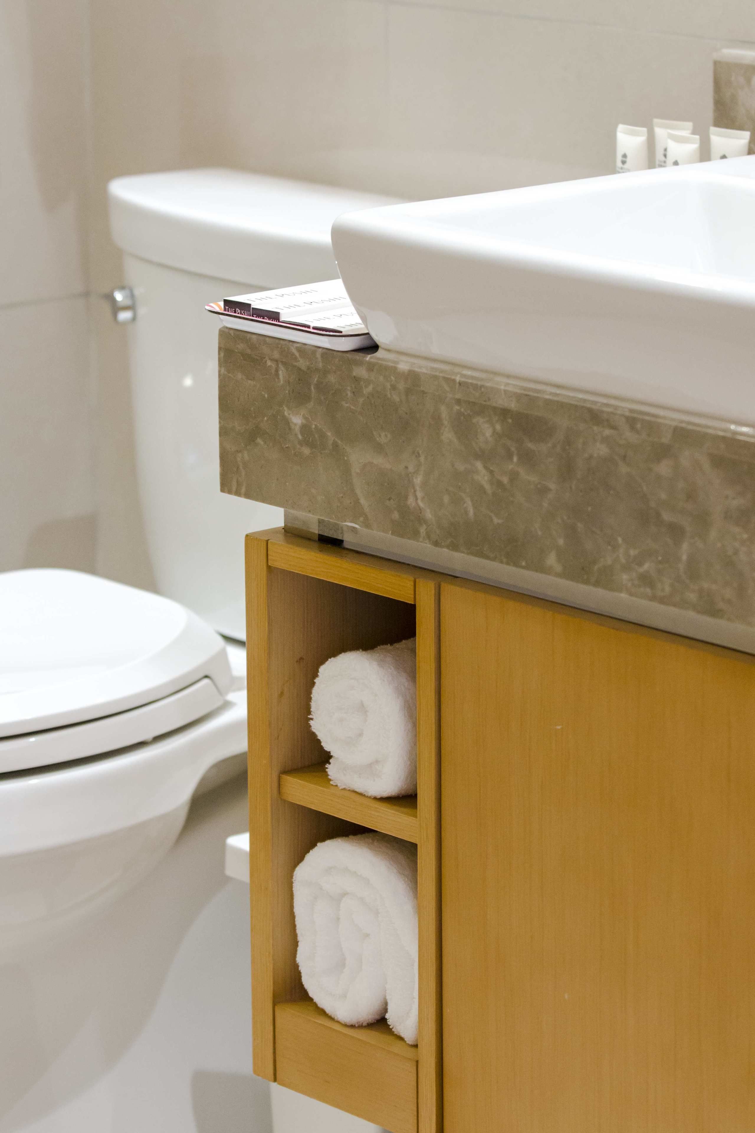 Een badkamer met een wit toilet, een marmeren aanrechtblad en een houten kastje met handdoeken.