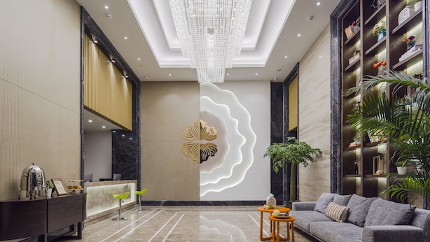 A spacious lobby with a modern chandelier, a reception desk, a grey sofa, and a decorative wall with a leaf pattern. - Pushi Serviced Apartment (Suzhou)