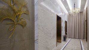 A modern hotel lobby with a marble floor, a gold decorative wall piece, a chandelier, and a view of the elevator. - Pushi Serviced Apartment (Suzhou)