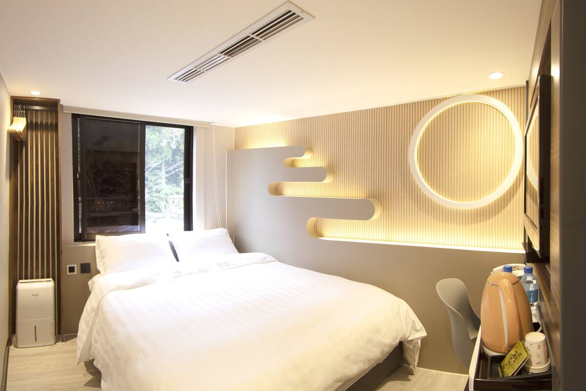 Une chambre d’hôtel moderne avec un grand lit, une table de chevet avec une lampe, un miroir et un luminaire circulaire encastré.