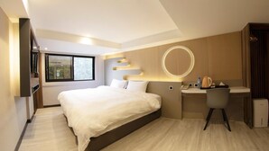 Une chambre d’hôtel moderne dotée d’un grand lit, d’un bureau avec une chaise, d’une petite kitchenette et d’une grande fenêtre offrant une vue sur l’extérieur.