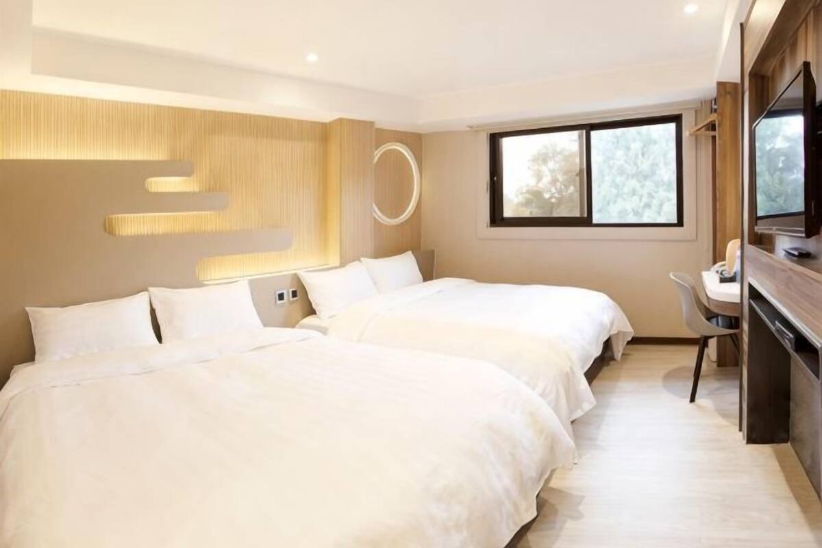 Une chambre d’hôtel avec deux lits, un bureau, une télévision et une grande fenêtre.