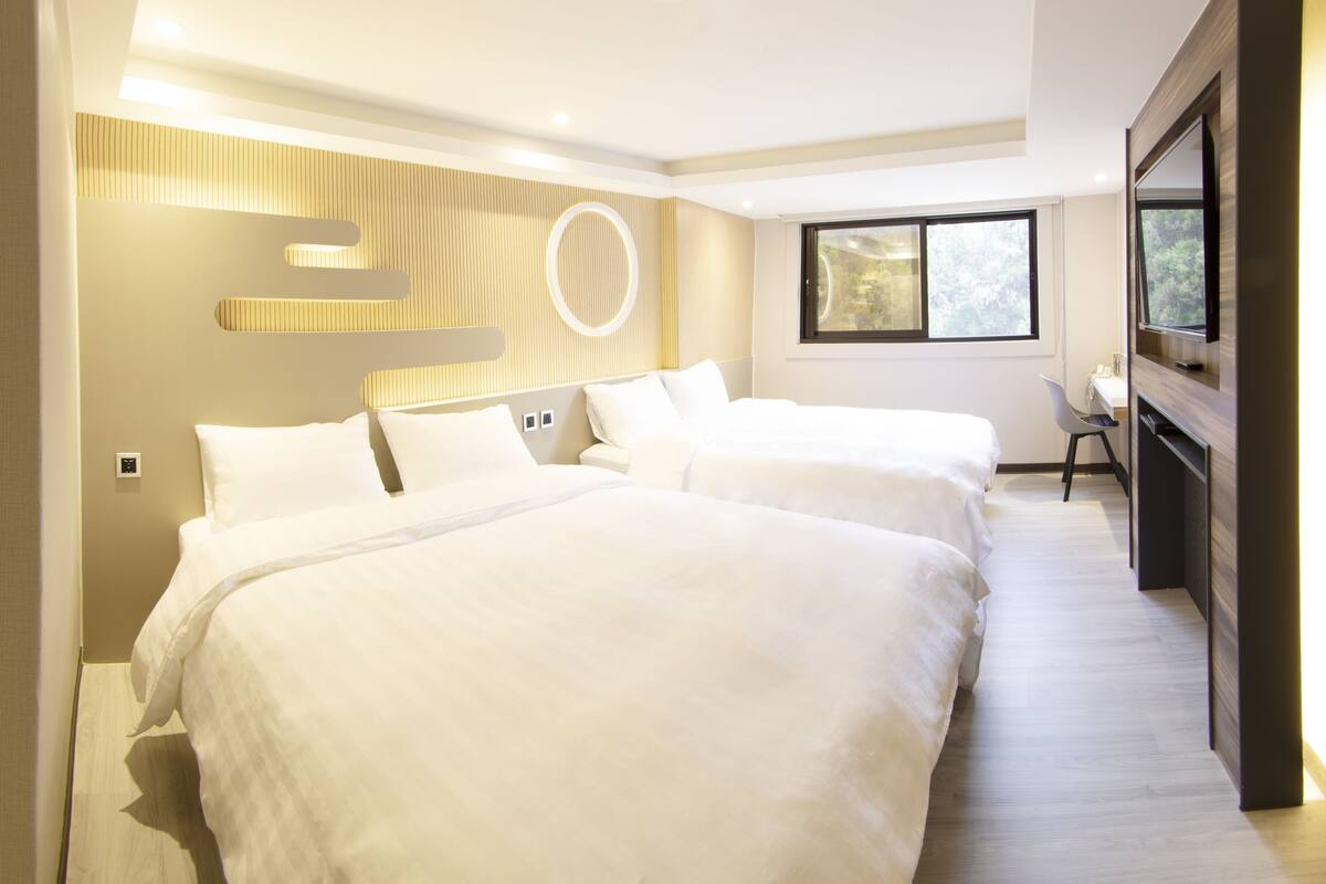 Une chambre d’hôtel avec deux lits, un bureau et une télévision.