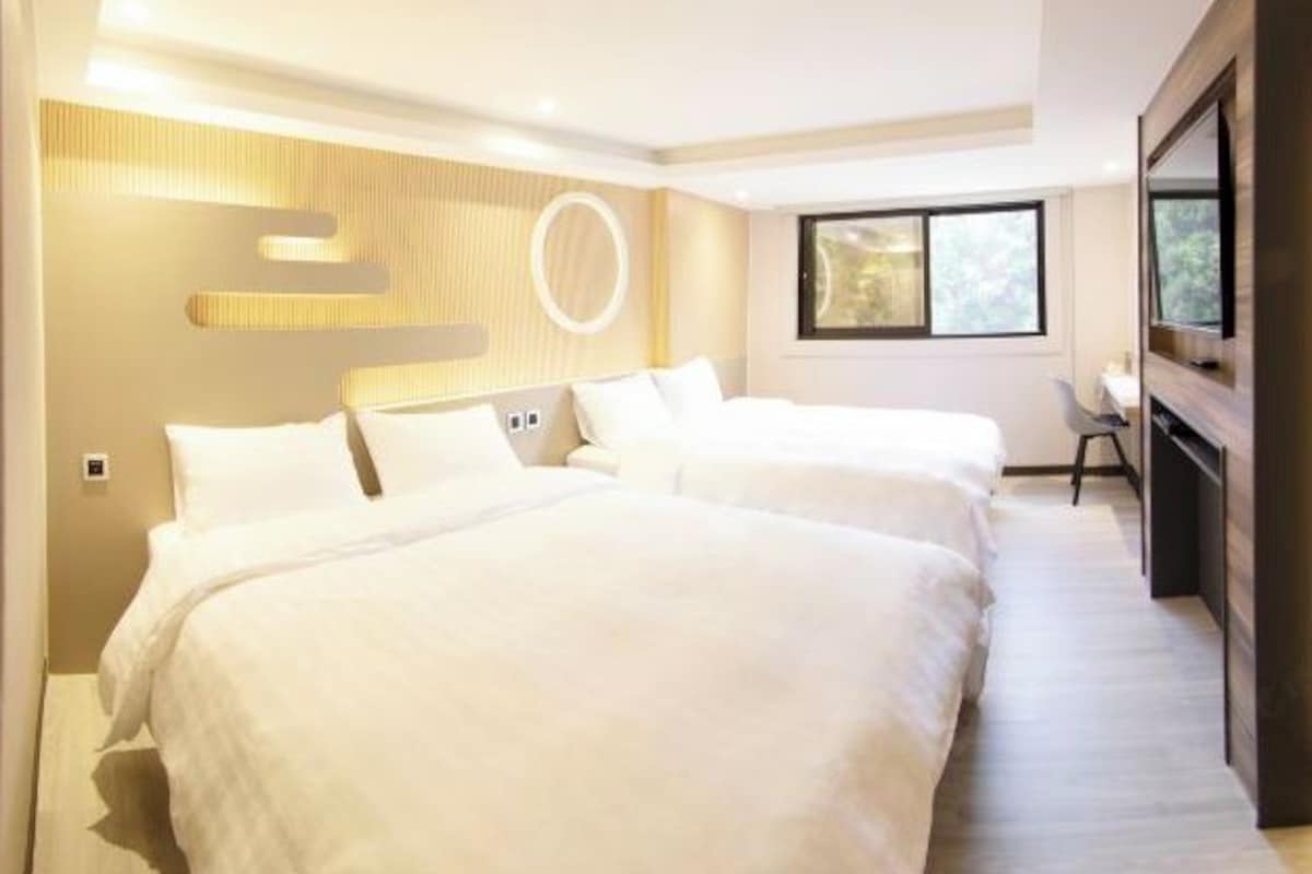 Une chambre d’hôtel avec deux lits, une télévision, un bureau et une fenêtre.