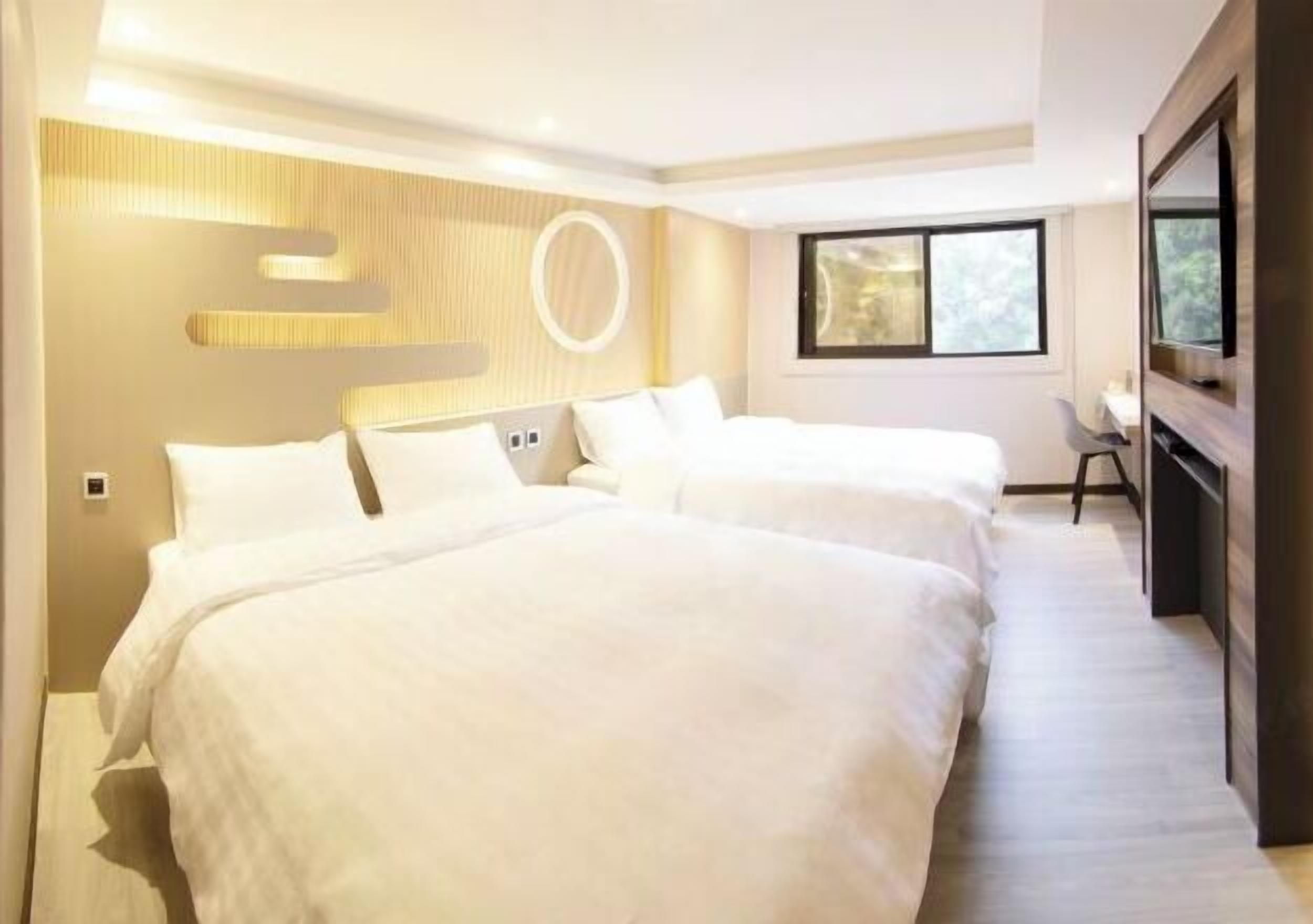 Ein Hotelzimmer mit zwei Betten, einem Fernseher, einem Schreibtisch und einem Fenster.