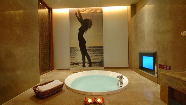 Ein Spa-Raum mit einer großen Badewanne, einer Holzabtrennung und einem digitalen Bildschirm an der Wand.