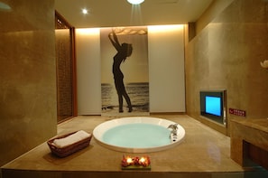Een spa-ruimte met een groot bad, een houten scherm en een digitaal scherm aan de muur.