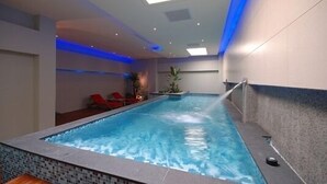 Ein Innenpool mit gefliestem Rand, einer Decke mit eingelassenen Leuchten und einer blauen Akzentwand.