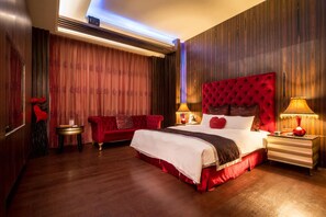 Une chambre d’hôtel avec un grand lit, un canapé rouge, une petite table et deux lampes de chevet.