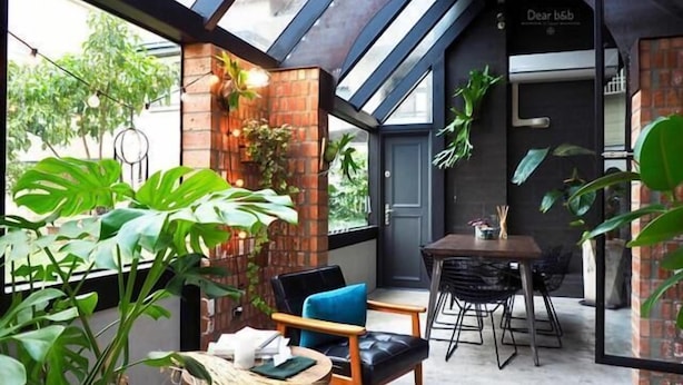 Un espacio interior acogedor con una pared de ladrillo, una mesa de comedor, sillas y plantas verdes exuberantes.