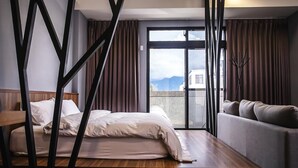 Habitación de hotel con cama, sofá, mesa de madera y vistas a montañas desde la ventana.