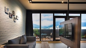 Una sala de estar moderna con un sofá, una mesa de centro y un televisor montado en la pared. Cuenta con un balcón con vistas a la ciudad y las montañas.