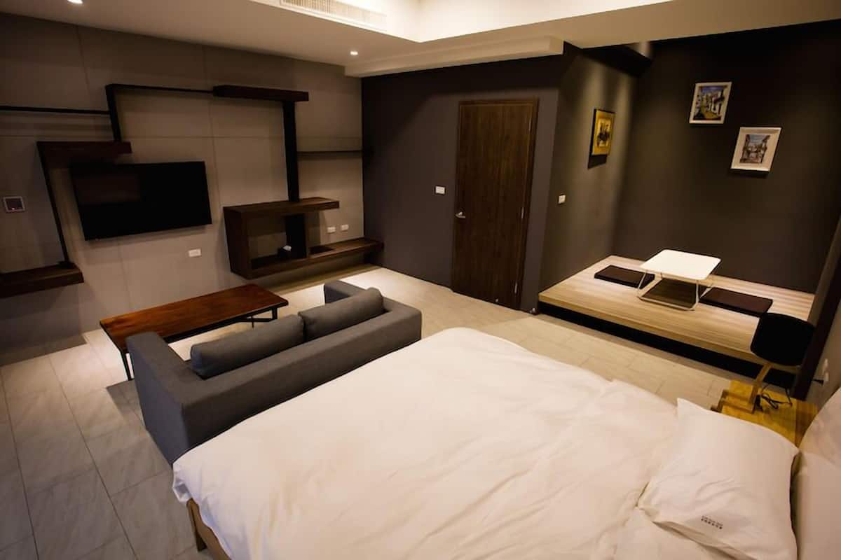 Un dormitorio moderno con una cama grande, un sofá, un televisor montado en la pared y un escritorio con una computadora portátil.