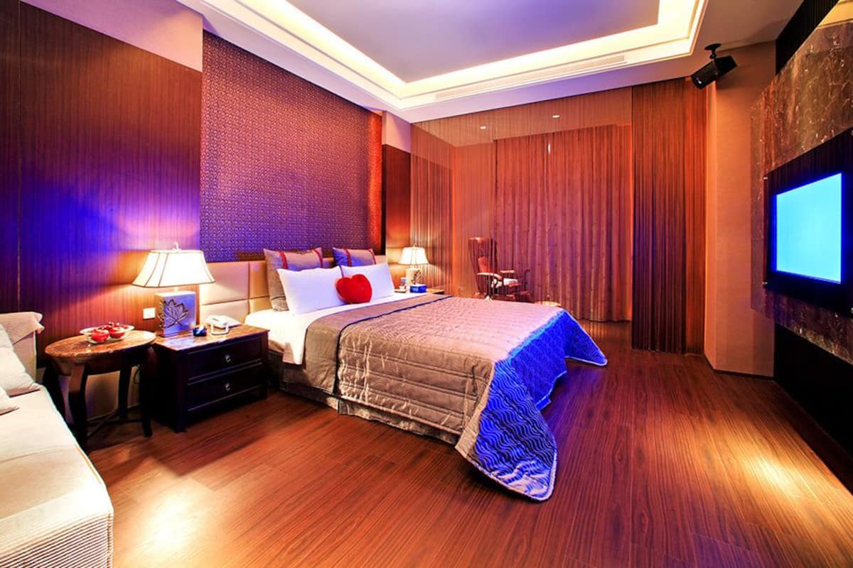 A modern hotel room with a large bed, two bedside tables, a TV, and a wooden floor.