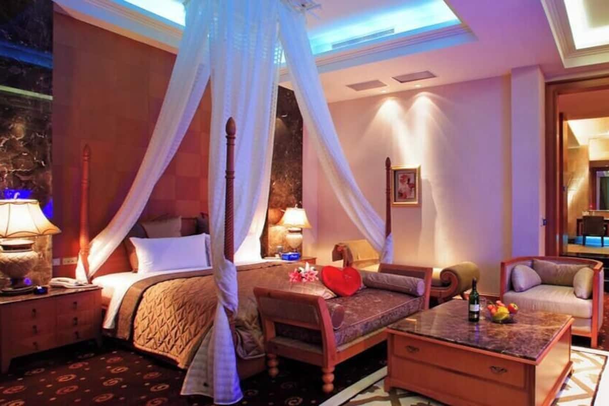 A luxurious bedroom with a canopy bed, a sitting area with a coffee table, and a television.